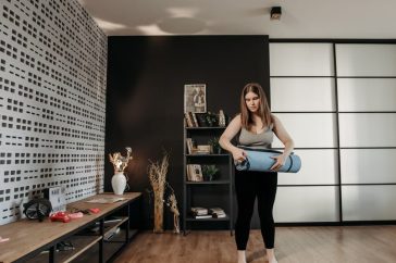 Plus size woman rolling a yoga mat in a stylish indoor setting with modern decor.