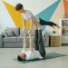 Happy couple is doing pair yoga at home, man is holding woman with legs on floor, girl is stretching arms. Relationship, active people and sports concept.